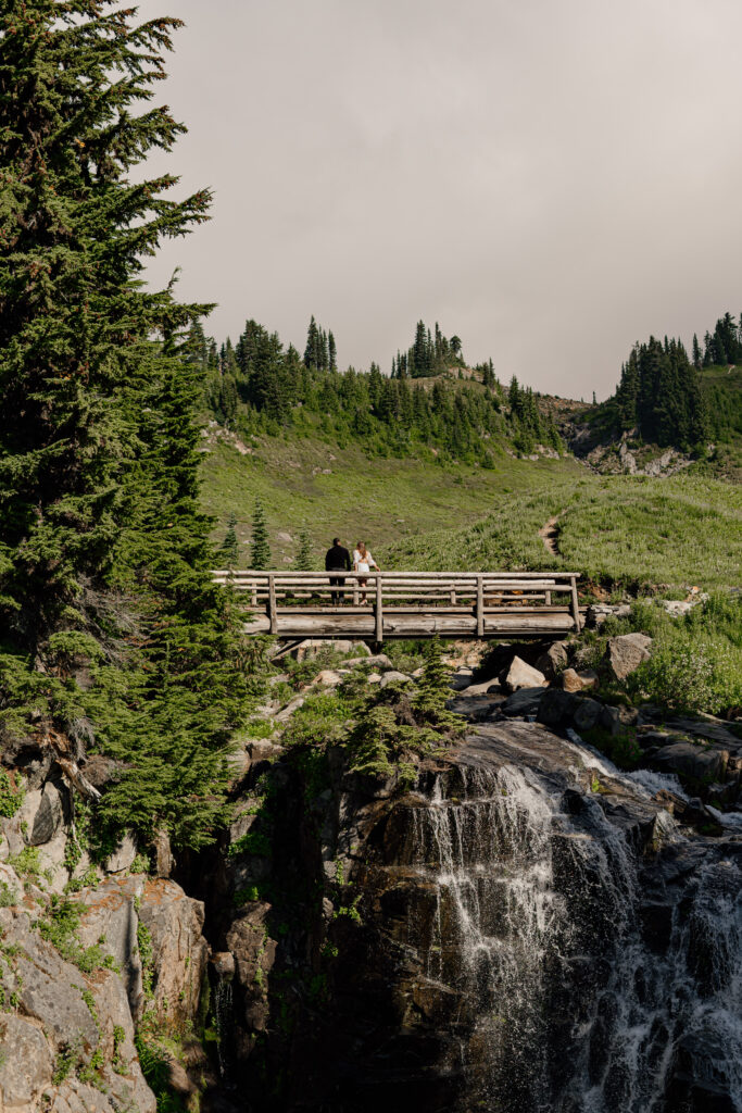 Couple standing on Myrtle Falls bridge at Mount Rainier National Park during their Adventure Engagement Session.