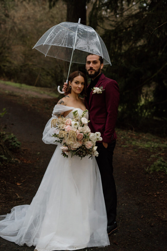 Couple in bridal attire with clear umbrella during their elopement at Hoyt Arboretum.