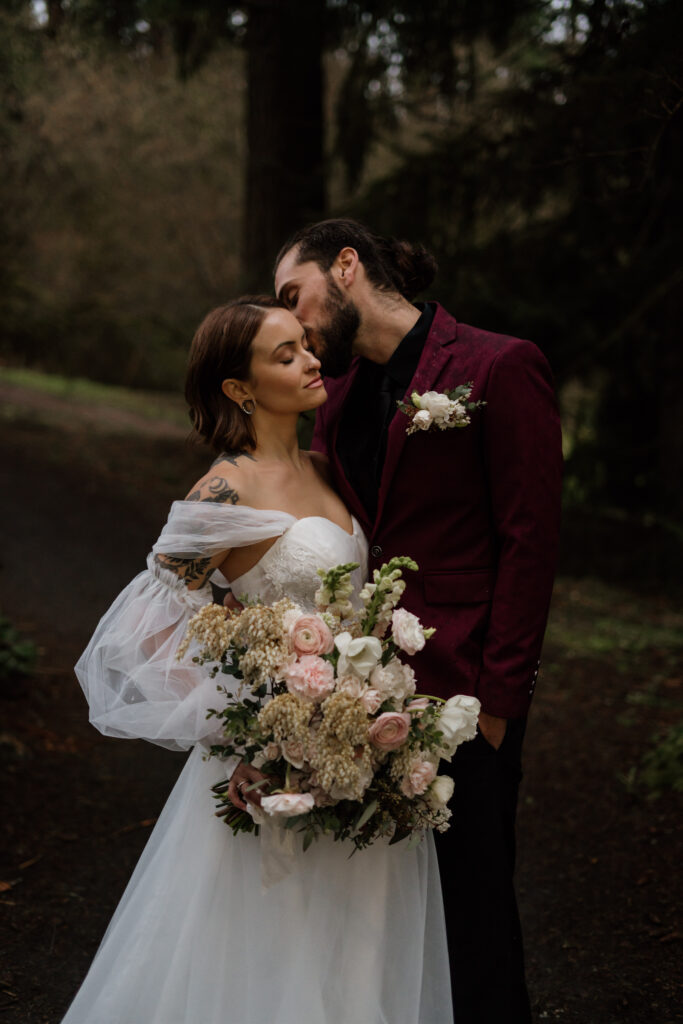 Groom kissing brides cheek during their twilight inspired elopement at hoyt arboretum in portland.