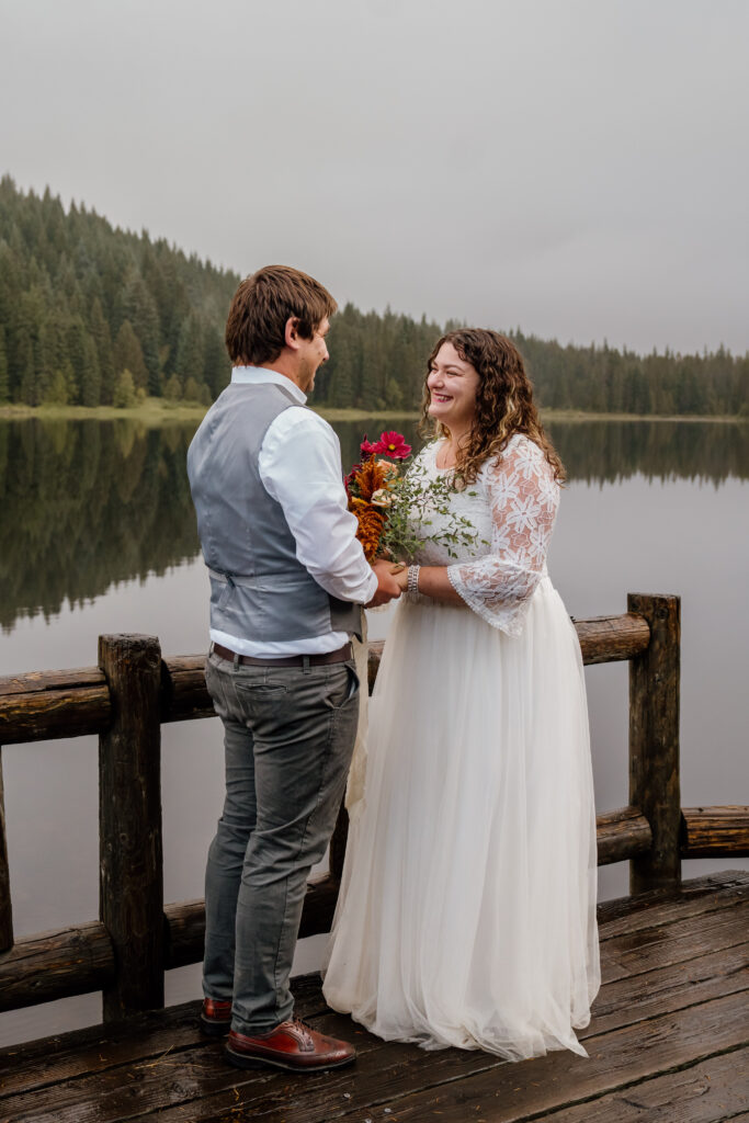 Bride and Groom holding hands and saying vows on the dock at Trillium Lake in Oregon after their sunrise canoe session.