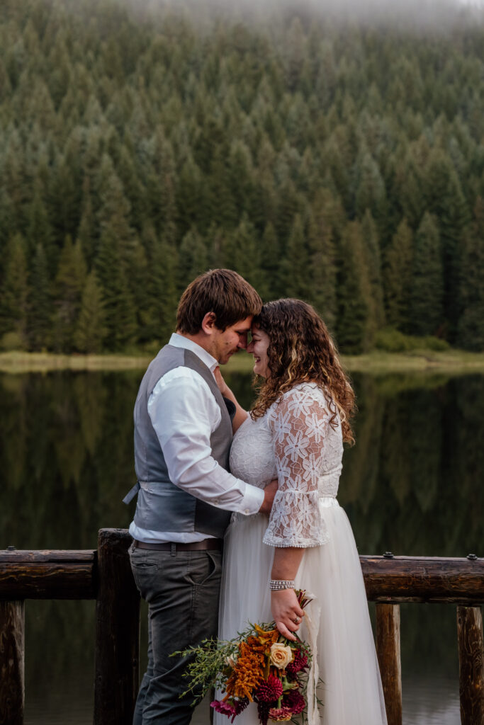 Couple snuggled in forehead to forehead after saying their vows on the dock at Trillium Lake in Oregon at their sunrise canoe elopement.