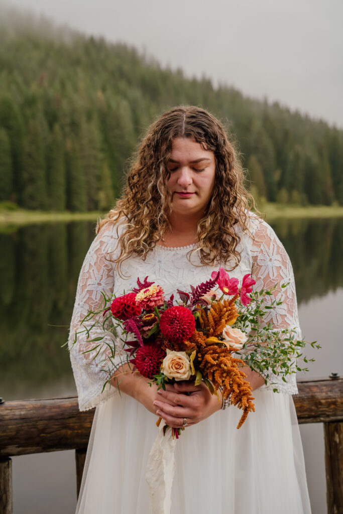 Bride holding her bridal bouquet on the dock at Trillium Lake in Oregon after her sunrise canoe elopement.