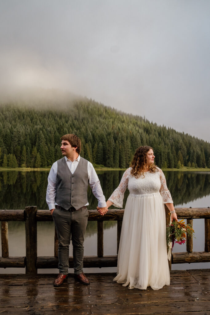 Bride and Groom holding hands and looking opposite directions, posing for Elopement photos on the dock at Trillium lake during their Trillium Lake Canoe Elopement.