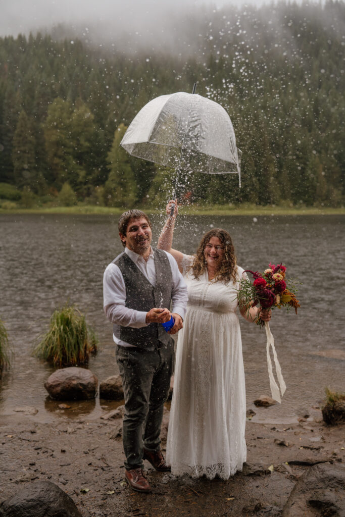 A joyous bride and groom during their champagne pop on their canoe elopement day at Trillium Lake, Oregon.