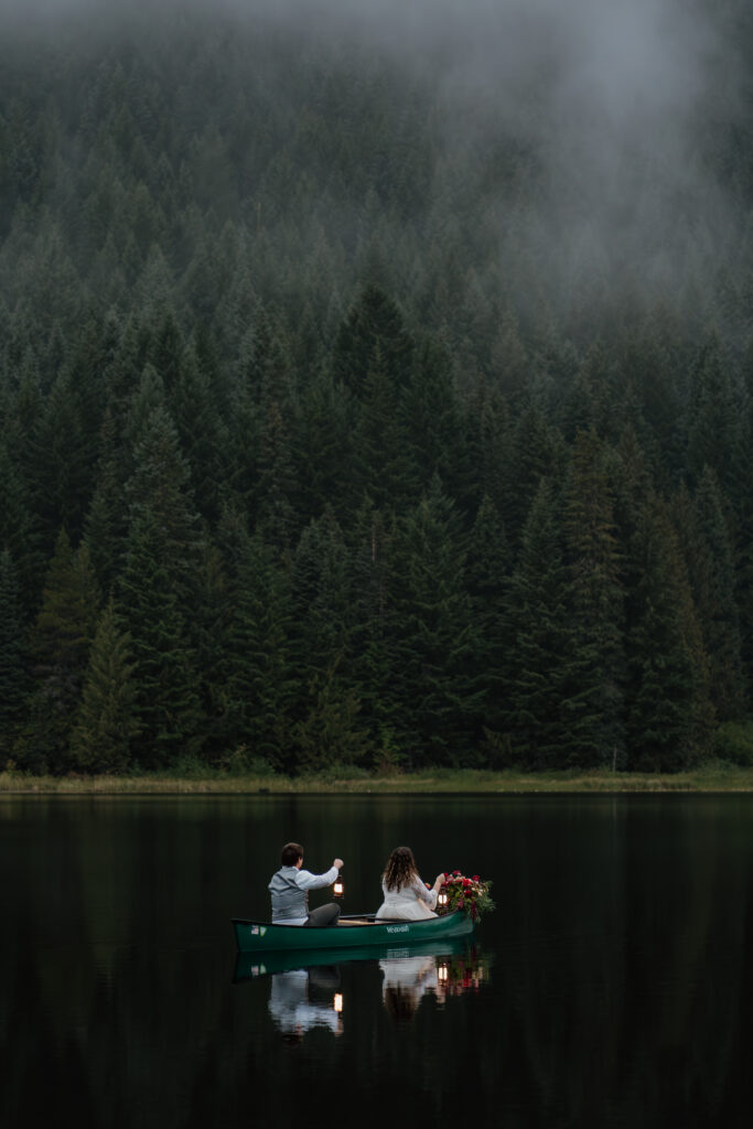 Bride and groom holding lanterns while canoeing during their sunrise canoe elopement on Trillium Lake in Oregon.