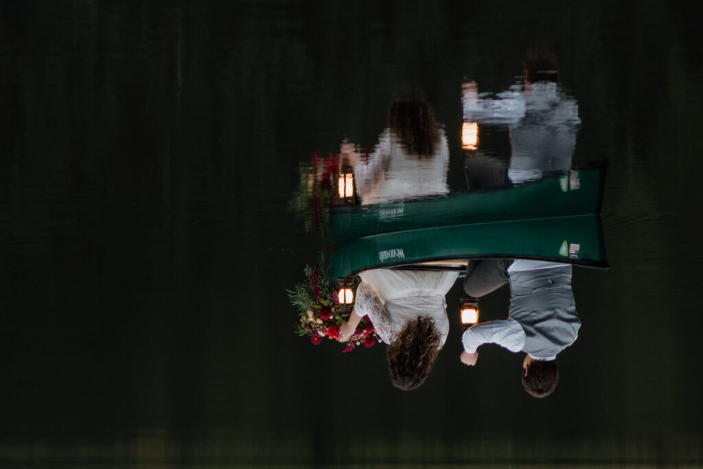 A flipped photo due to a perfect reflections of a dride and groom holding lanterns while canoeing during their sunrise canoe elopement at Trillium Lake in Oregon.