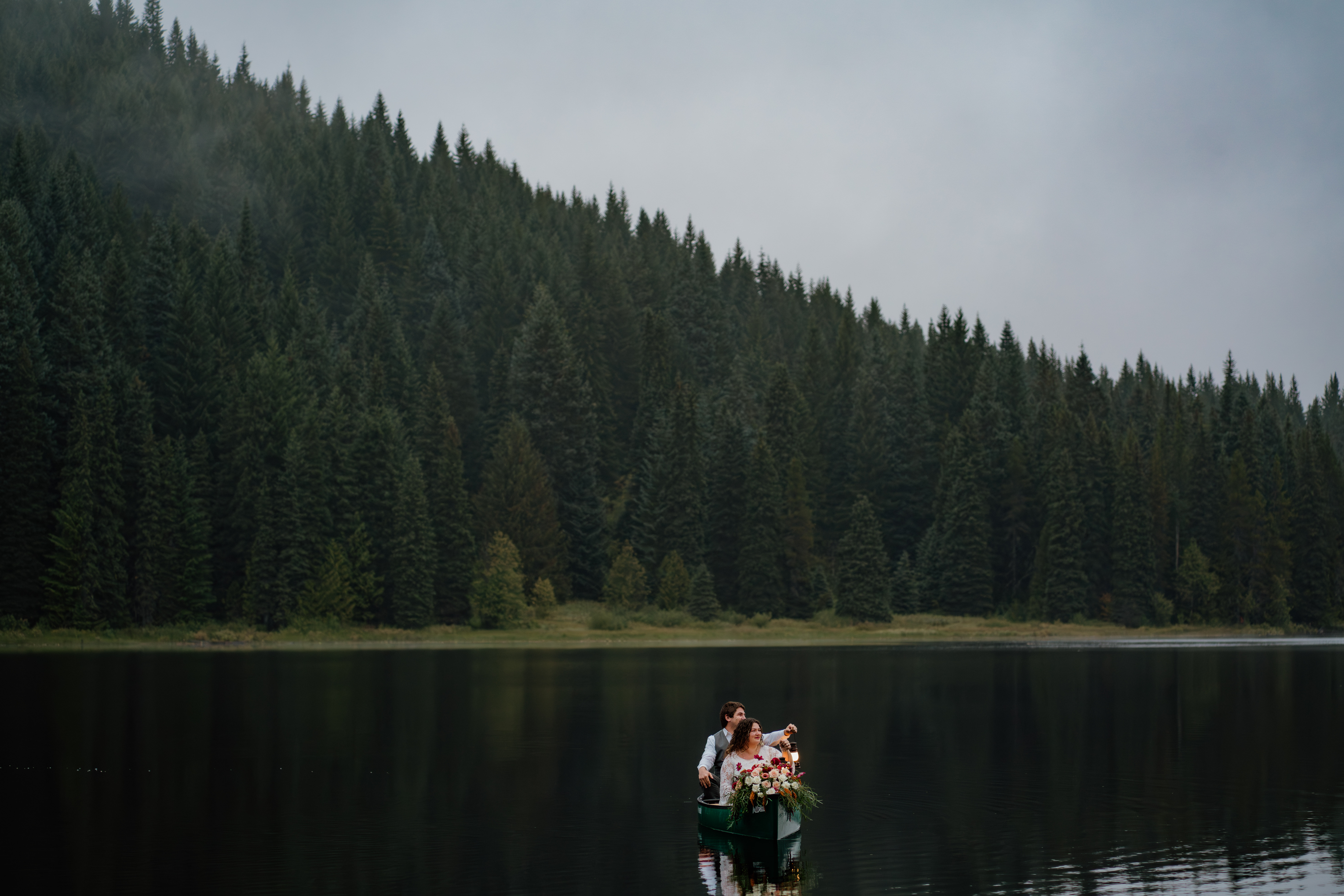 Couple holding lanterns while canoeing on Trillium Lake in Oregon during their sunrise elopement.