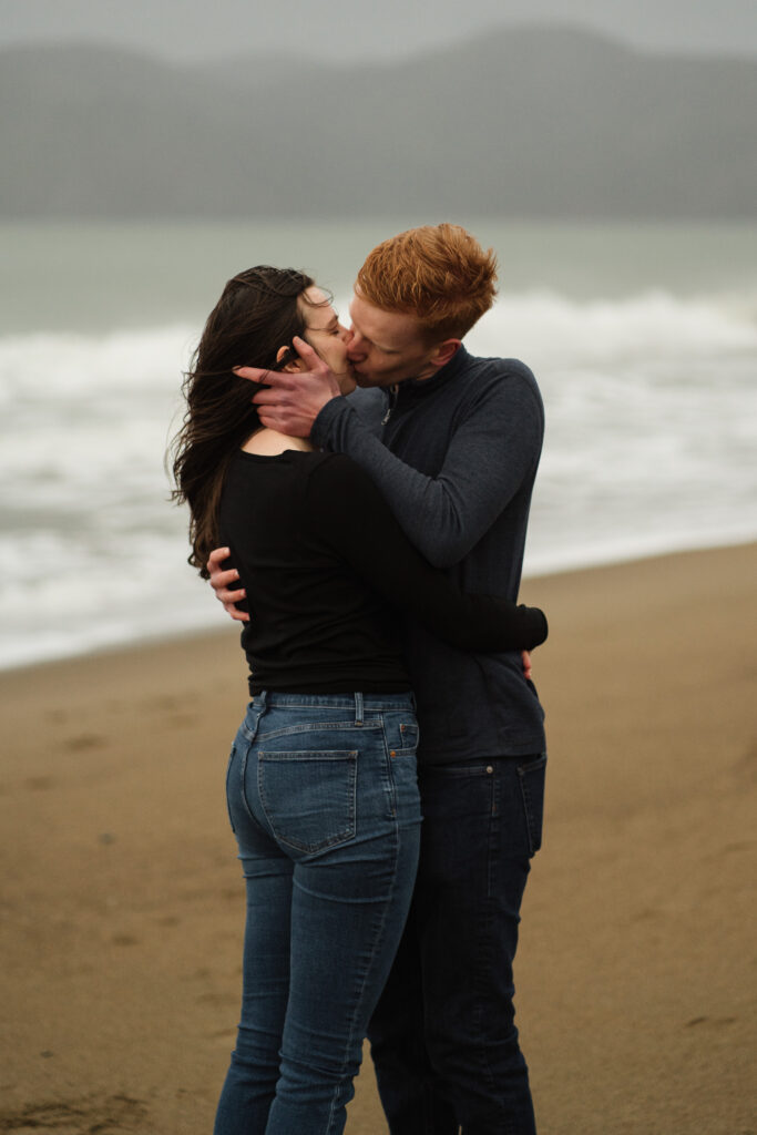 Couple kissing at Baker Beach during their engagement photos session with Before Our Eyes Photography.