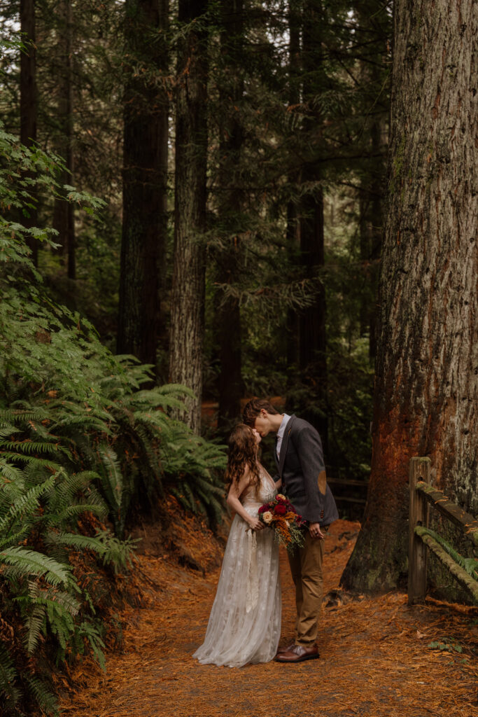 Couple standing on trail and kissing while holding bridal bouquet during their Hoyt Arboretum Elopement.