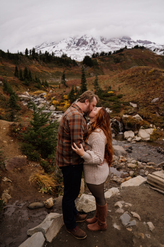 Couple kissing while on a hiking trail at Mount Rainier National park surround by the fall colors.