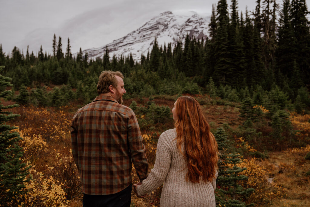 Couple looking at eachother with backs to camera during their Mount Rainier NP adventure engagement session.