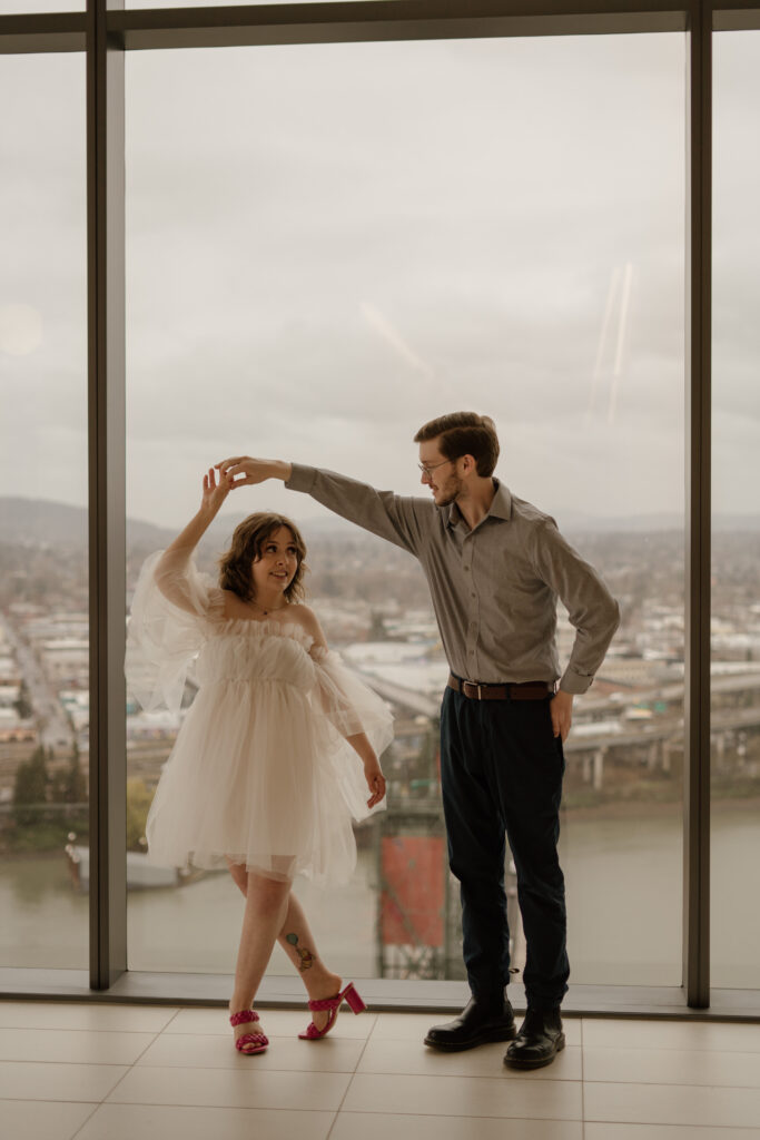 Couple dancing in front of large windows overlooking Portland Oregon from the Multnomah County Courthouse.