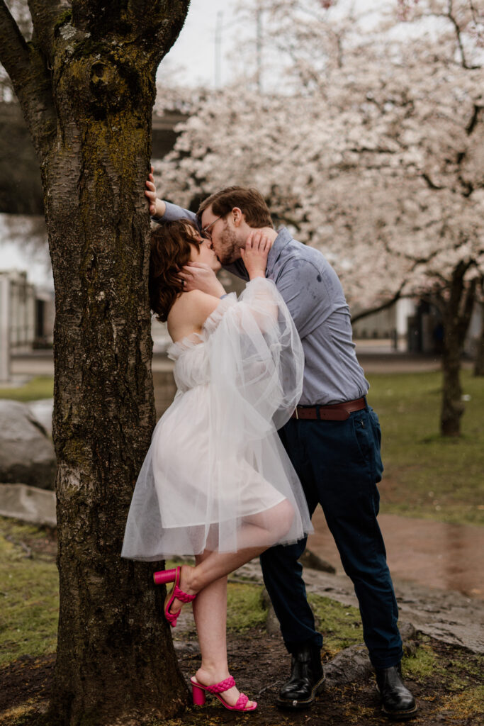 Couple kissing against a blooming cherry tree after their Portland Elopement.
