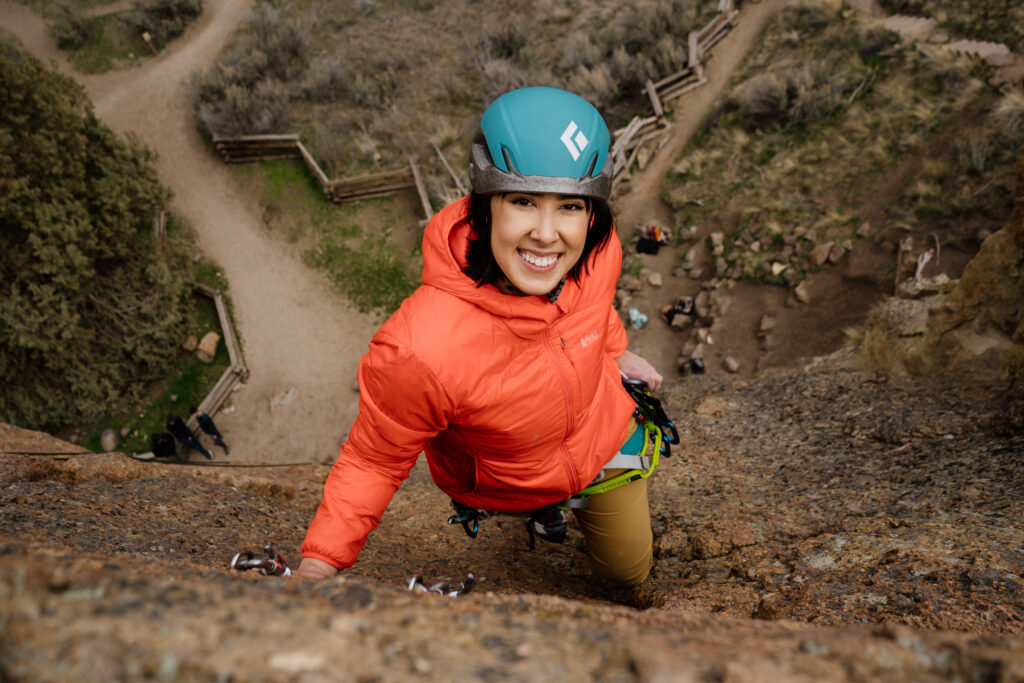 Woman looking up at camera while climbing during a couples adventure climbing session at Smith Rock State Park