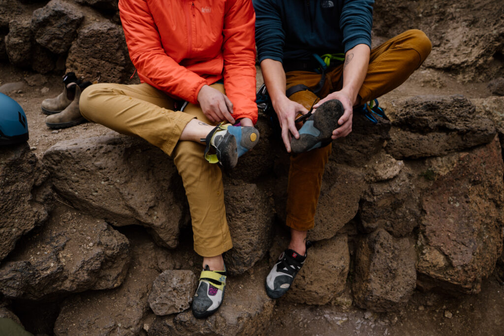 Couple sitting side by side getting their climbing shoes on during their climbing adventure session.