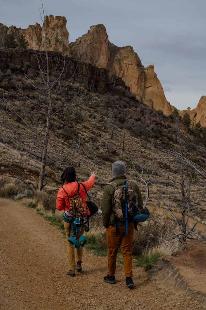 Couple walking with gear and pointing at climbing crag during their Climbing Adventure Session at Smith Rock State Park