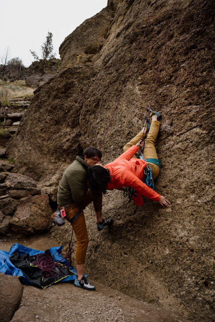 Couple kissing in spiderman pose during their couples climbing photos at Smith Rock State Park in Oregon.