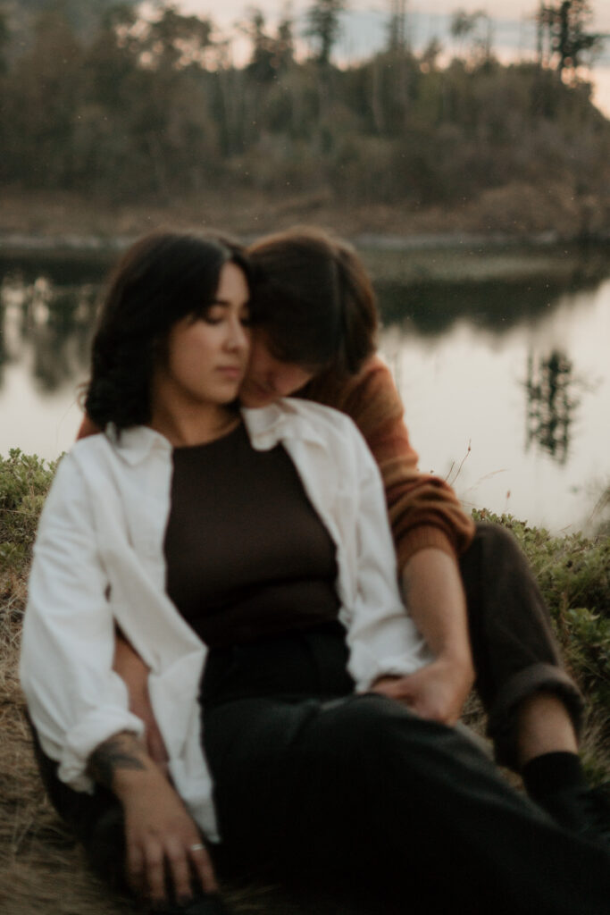 Couple snuggled in sitting on the ground at Government cove during their engagement photos.