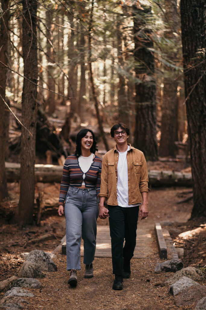 Couple holding hands and walking down a trail at Trillium Lake during their engagement photos.