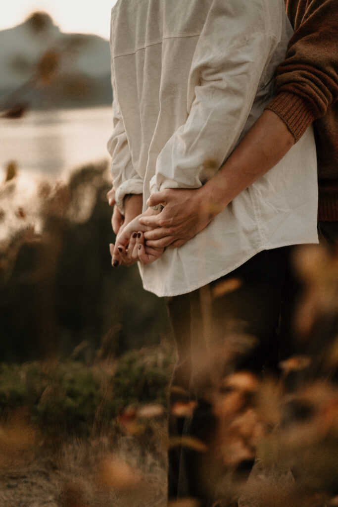 Close up photo of a couples hands with the Columbia River Gorge in the background see from Government Cove.