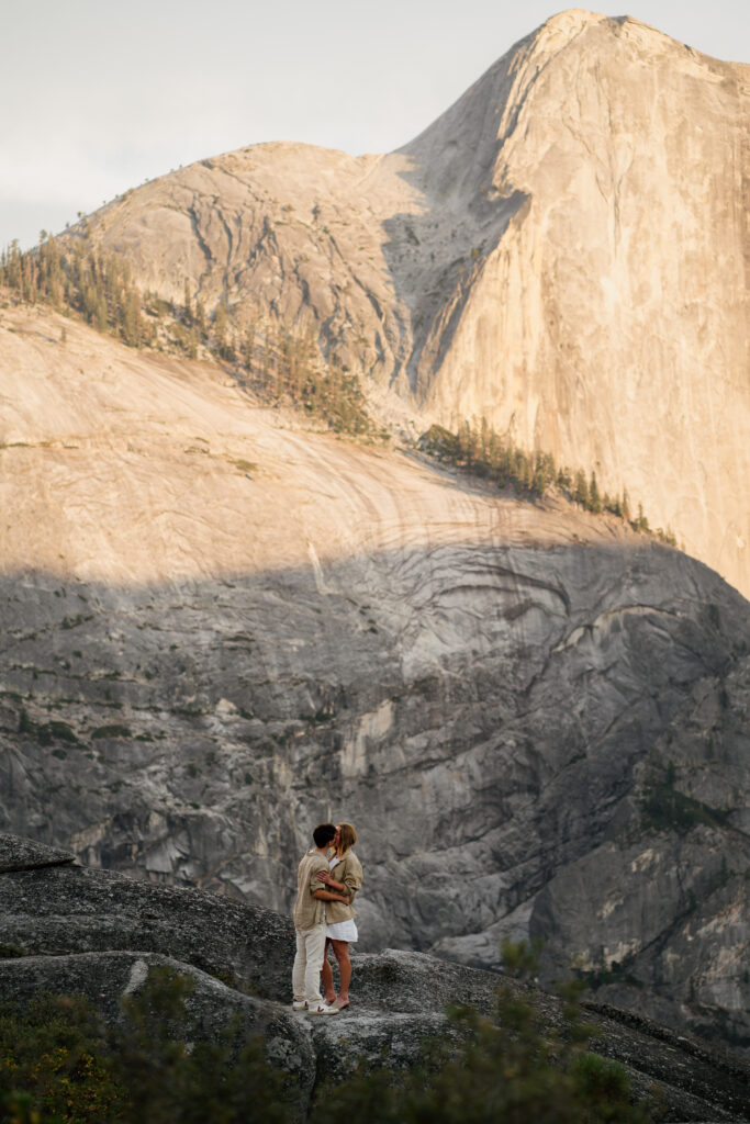 Photo of couple small in the foreground with Half Dome towering over them in the background.