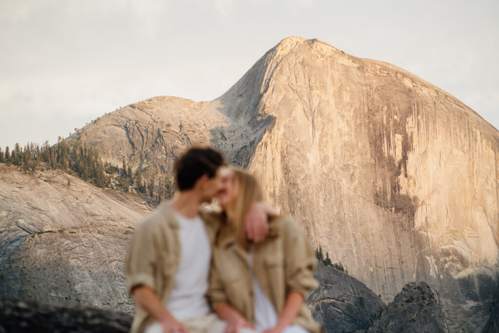 Couple kissing out of focus with Half Dome in Yosemite National park in focus in the background.