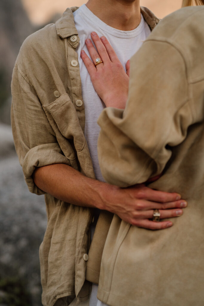 Close up photo of woman wearing engagement ring with hand on her fiancee's chest after being proposed to a Yosemite National Park.