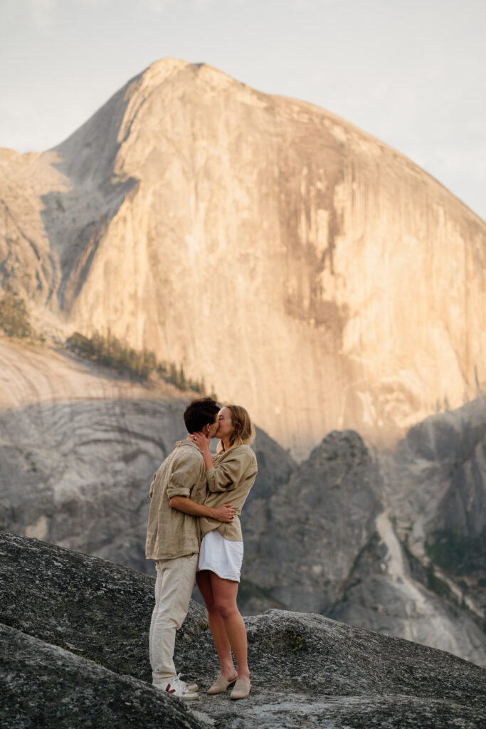 Couple kissing with Half dome in the background at their Yosemite National Park engagement photos.