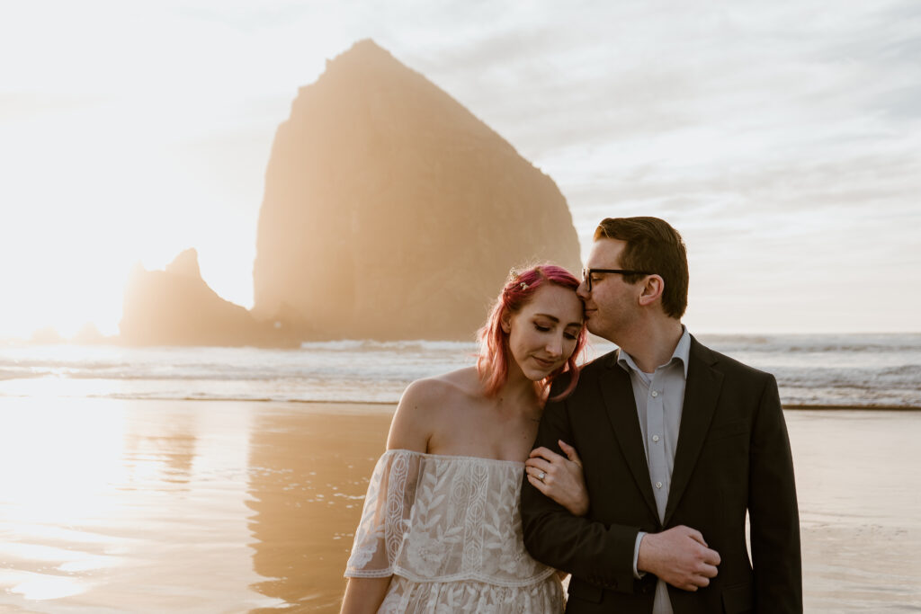 Groom kissing brides head while exploring Cannon Beach on their Elopement day.