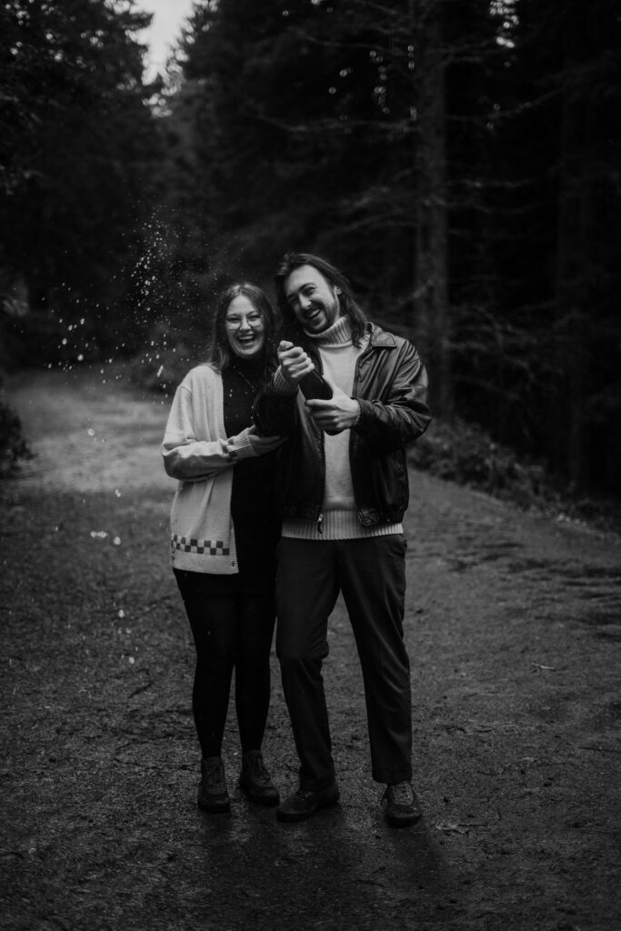 Couple doing a champagne pop during their engagement photos at Hoyt Arboretum in Portland Oregon.