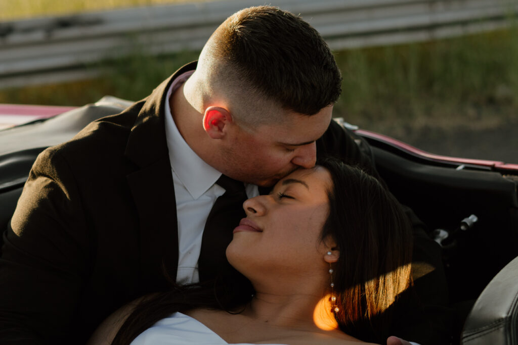 Man kissing woman's forehead while snuggled into the backseat of a vintage ford mustang during their engagement session.