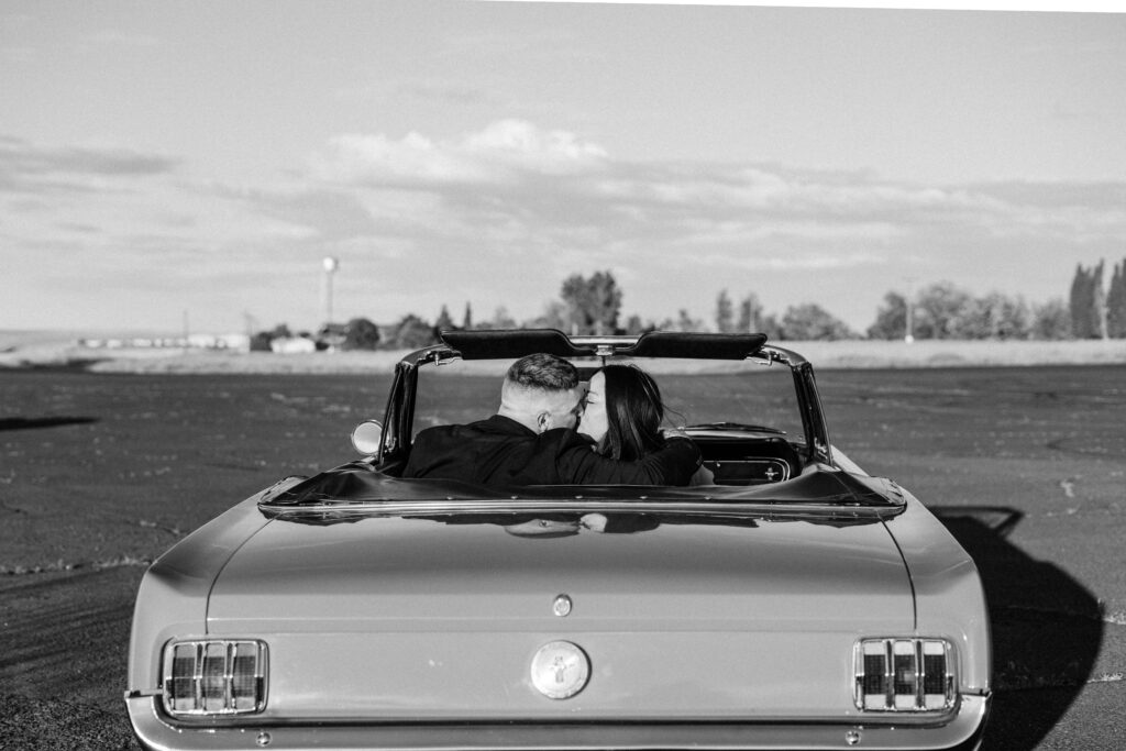 Black and white photo of couple kissing while sitting in the back of a classic ford mustang during their Columbia River Gorge Vintage Car engagement session.