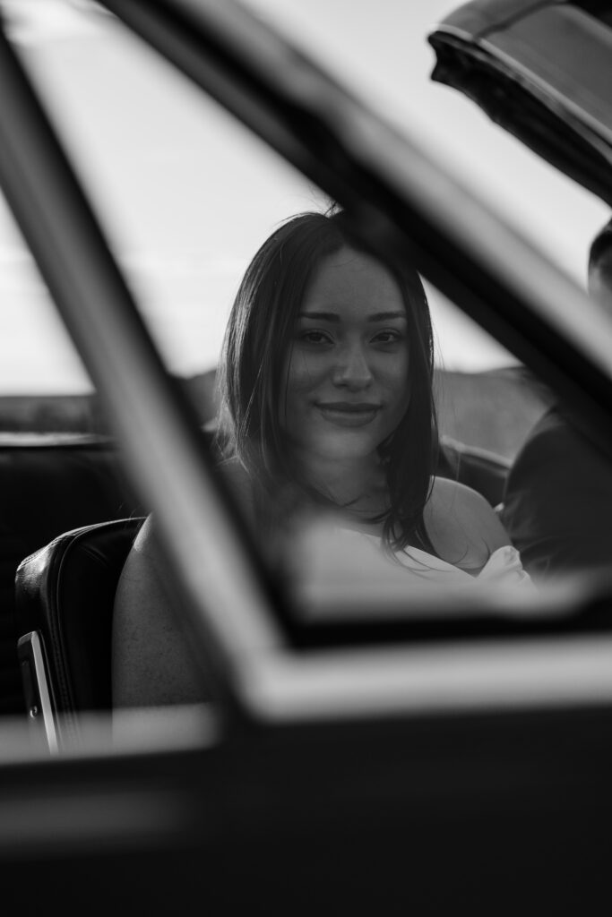 Woman through the small glass door window on a classic ford mustang during her Columbia River Gorge vintage car engagement session.