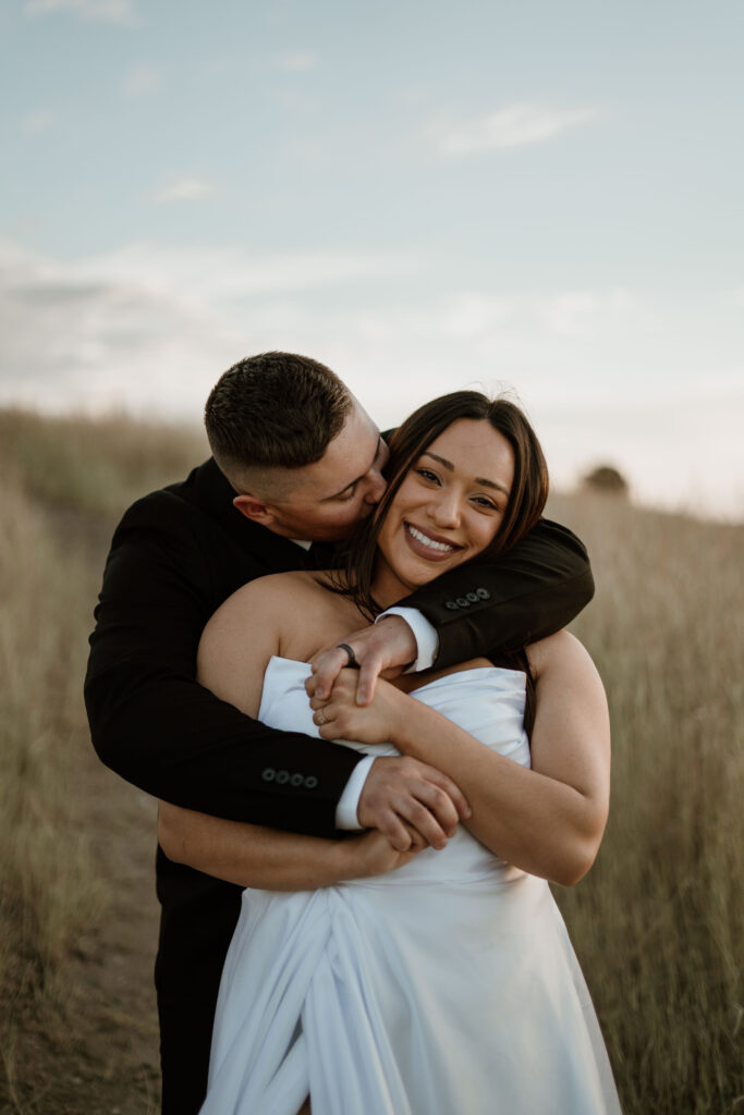 Man hugging woman from behind with her smiling at camera for engagement photos.