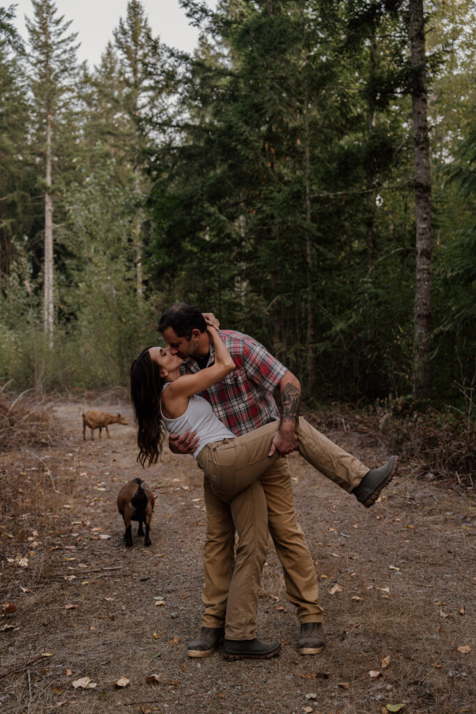 Man dipping woman for a kiss surrounding by goats during their engagement photos.