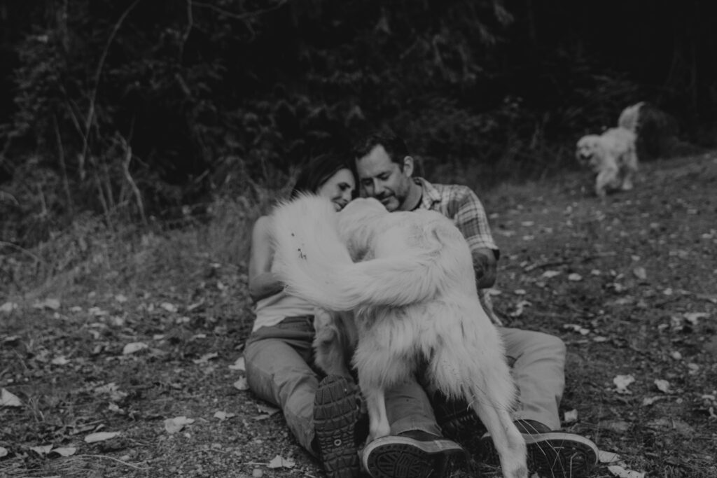 b+w photo of couple sitting on the ground giving their dog some pets during their Seattle engagement session.