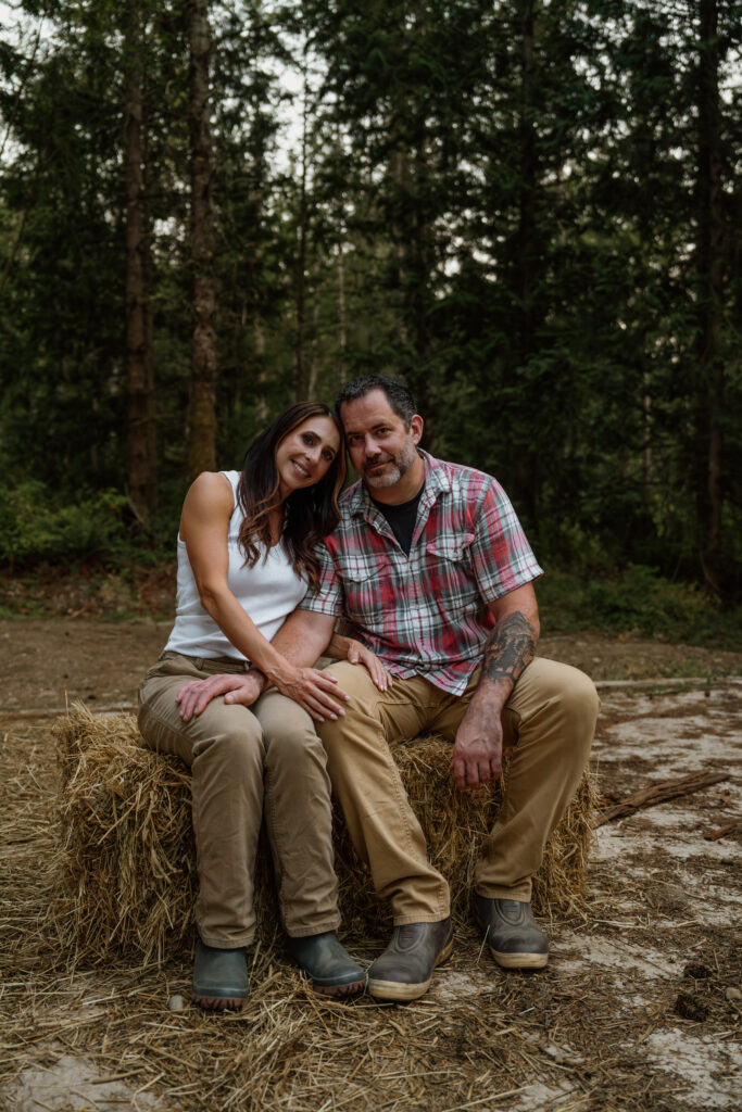 Couple sitting on hay bail during their engagement session which included goats and dogs.