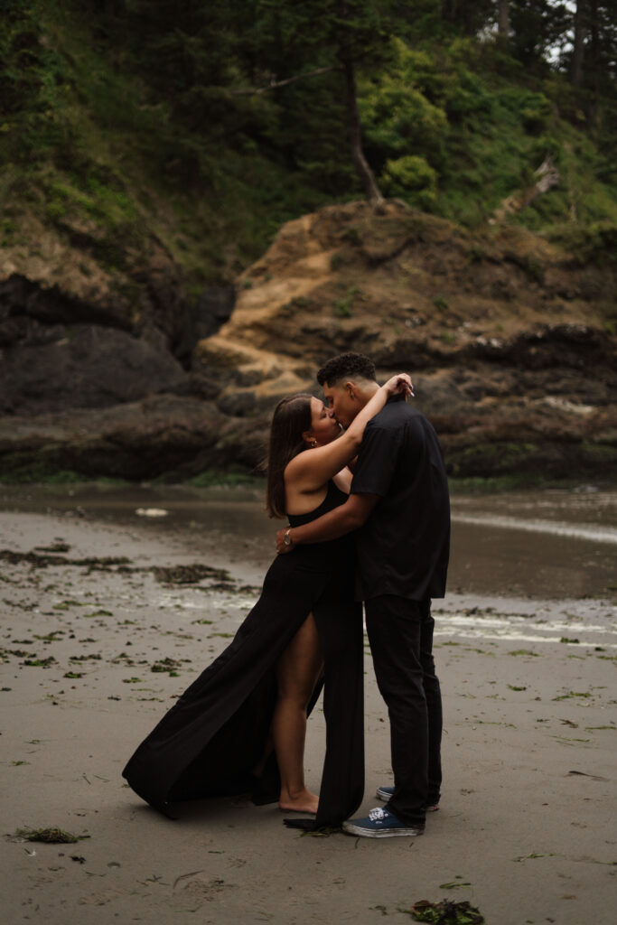 Couple standing and kissing with the wind blowing the woman's dress during their engagement session on the Washington Coast.