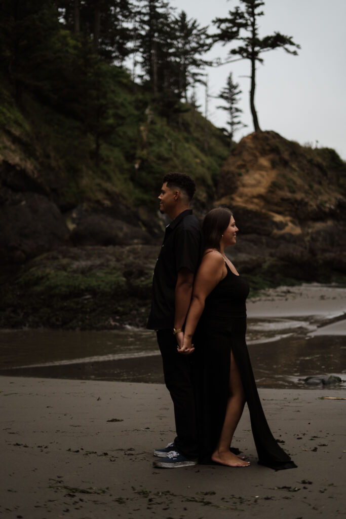 Couple standing back to back on the beach.