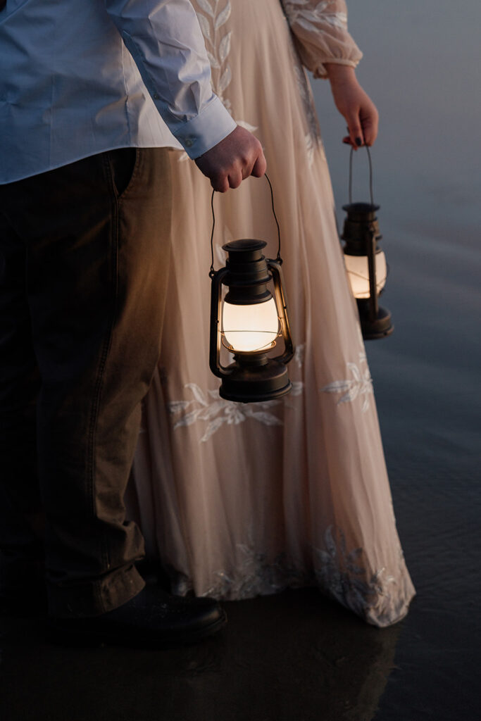 Couple in elopement attire holding lanterns while hanging out on Arcadia Beach in Oregon.