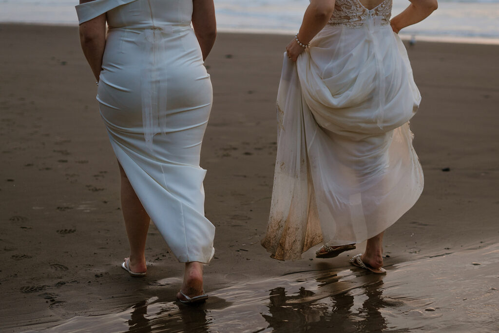 Close up of brides dirty wedding gowns as they walk along the sandy shore