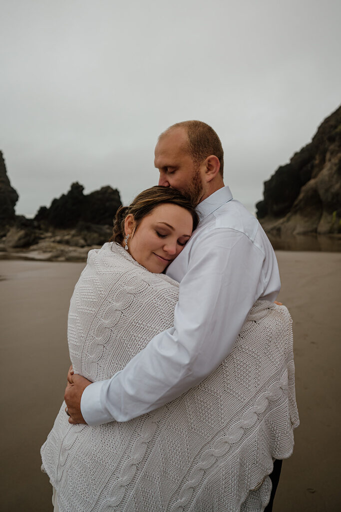 Couple snuggles up on the beach with a knit blanket