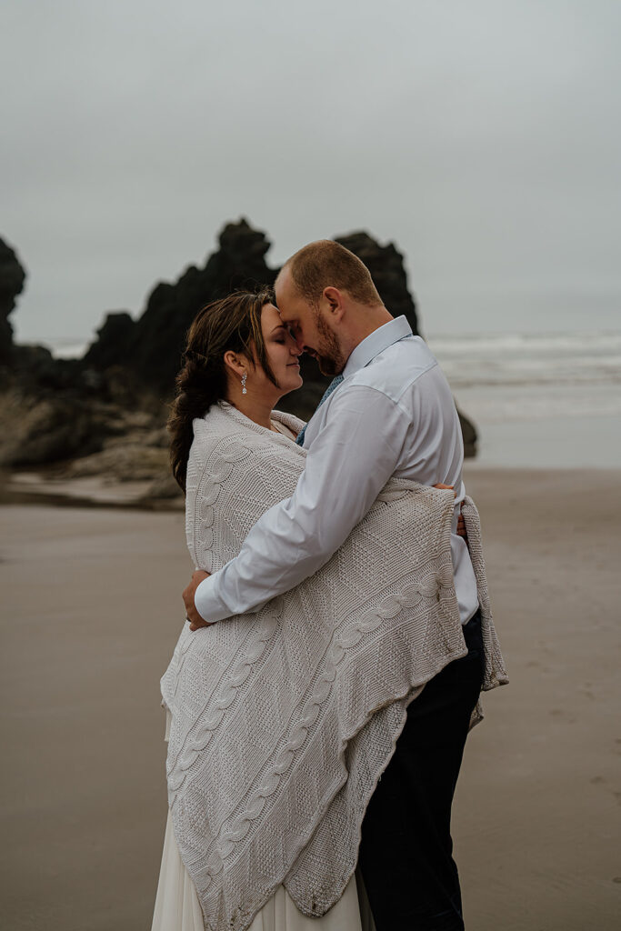 Couple snuggles up on the beach with a knit blanket