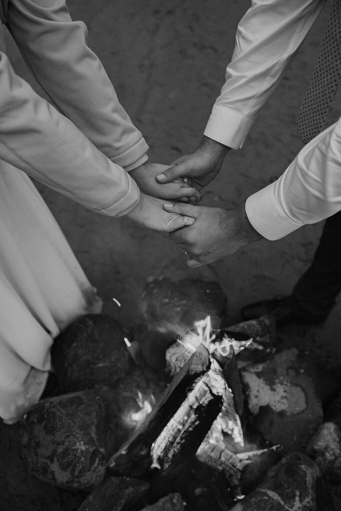 Bride and groom warm their hands above the crackling fire