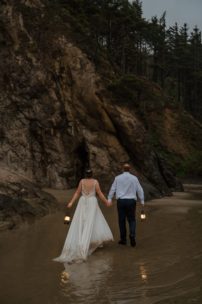 Bride and groom walk along the sandy shore with lanterns