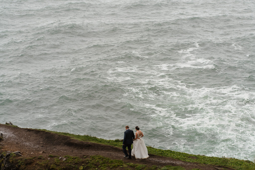 Bride and groom walk along Elk Flats cliffs with the Pacific Ocean in the backdrop