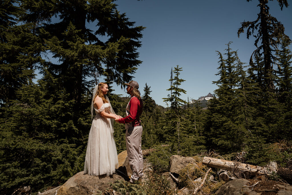 Bride and groom stand on a boulder atop a mountain during their Oregon adventure elopement ceremony vows