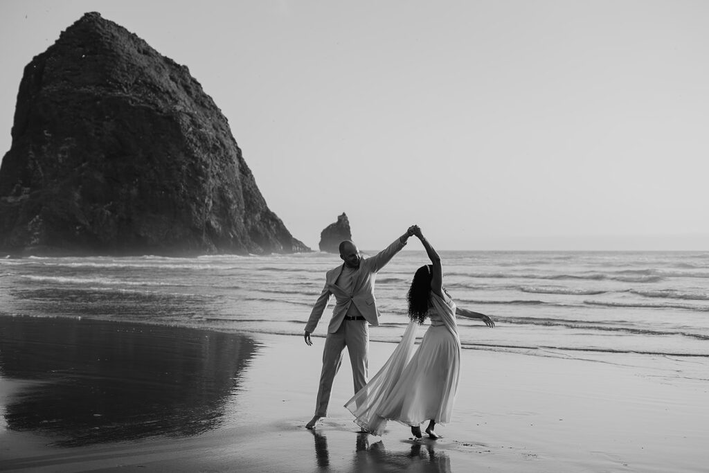 Couple dancing around with Haystack Rock in the backdrop for their Cannon Beach bridal portraits.