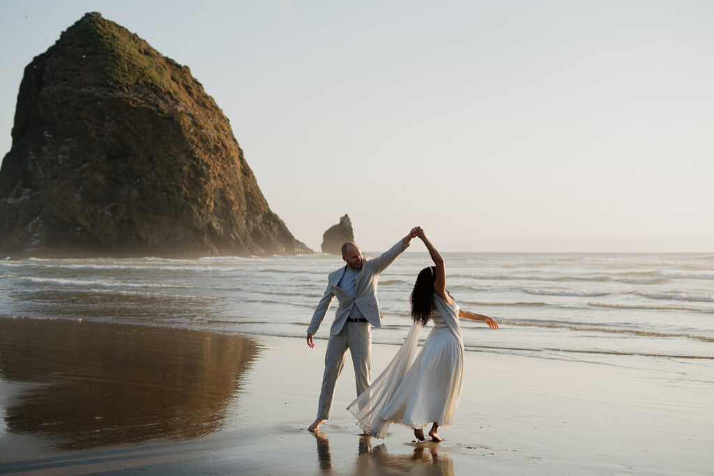 Couple dancing around with Haystack Rock in the backdrop for their Cannon Beach bridal portraits.