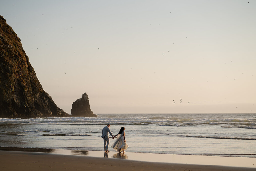 Couple walking into the ocean with Haystack Rock in the backdrop for their Cannon Beach bridal portraits.